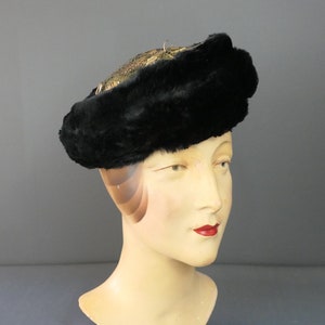 May include: A black fur hat with a gold trim. The hat is worn on a mannequin's head.