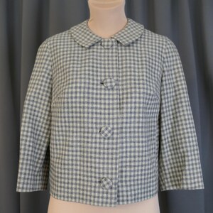 May include: A vintage-style jacket in a blue and white gingham pattern. The jacket features a rounded collar, three large matching buttons, and three-quarter sleeves. The jacket is displayed on a mannequin against a gray backdrop.