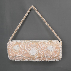Op de afbeelding: Een vintage, blush-gekleurde, met kralen bezette handtas met een bijpassende kralenriem. De rechthoekige clutch heeft ingewikkelde witte bloempatronen en een overslag. De riem is ongeveer 51 cm lang.