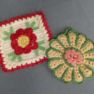 May include: Two handmade crochet items: a square trivet with a red rose and a round, flower-shaped trivet. The square trivet has a white center with a red border and green leaves. The round trivet is tan, green, and pink.