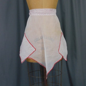 May include: White apron with red polka dots and a scalloped edge. The apron has two pockets on the sides.