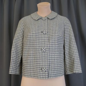 May include: A vintage-style jacket in a blue and white checkered pattern. The jacket has a rounded collar, three large matching buttons, and three-quarter sleeves. The fabric appears to be a woven material.