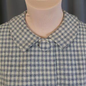 May include: A vintage-style coat in a blue and white checkered pattern. The coat features a classic collar and a single button closure. The fabric has a textured appearance, suggesting a wool or similar material.