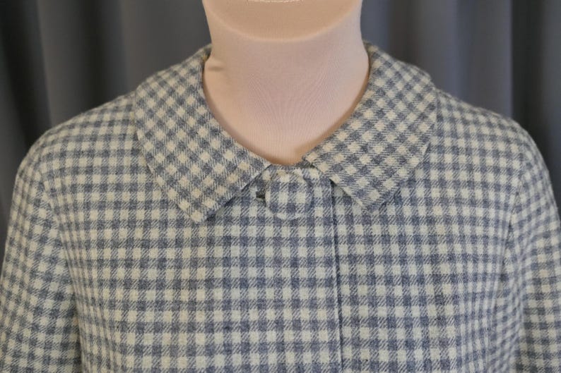 May include: A vintage-style coat in a blue and white checkered pattern. The coat features a classic collar and a single button closure. The fabric has a textured appearance, suggesting a wool or similar material.