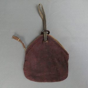 May include: A burgundy suede pouch with a zipper closure and a small handle. The pouch has a circular metal ring attached to a leather strap. A small tassel hangs from the side.