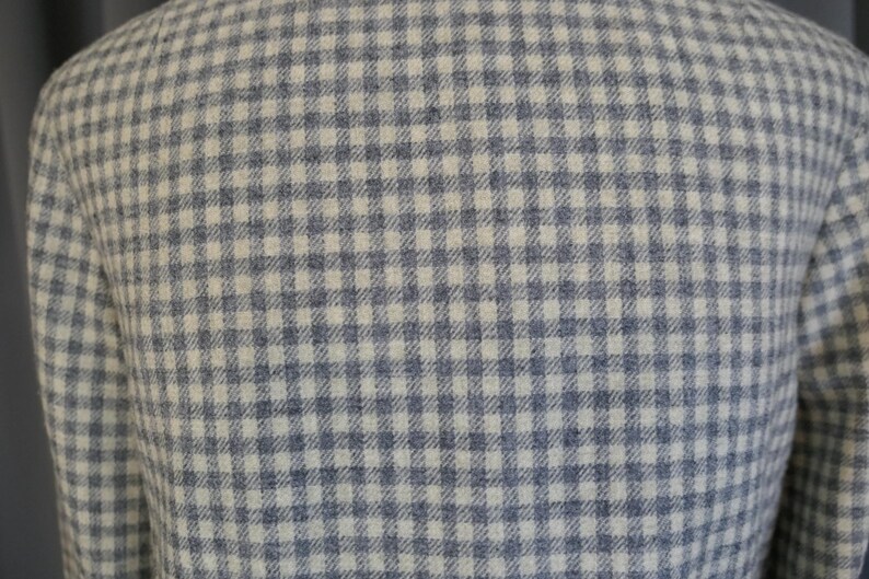 May include: Close-up of a jacket with a blue and white checkered pattern. The fabric has a textured appearance, and the pattern is evenly distributed across the garment. The jacket appears to be made of a woven material.