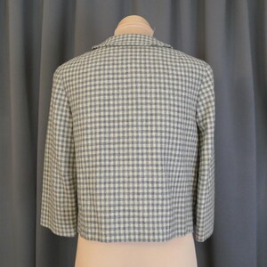 May include: A cropped jacket in a light blue and white checkered pattern. The jacket has three-quarter sleeves and a notched collar. The back of the jacket is displayed on a mannequin. The fabric appears to be a woven material.