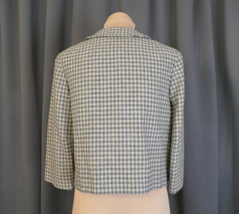 May include: A cropped jacket in a light blue and white checkered pattern. The jacket has three-quarter sleeves and a notched collar. The back of the jacket is displayed on a mannequin. The fabric appears to be a woven material.