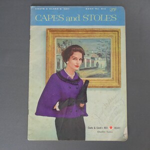May include: Vintage magazine cover titled "Capes and Stoles" featuring a woman in a purple cape and black gloves. The cover has a painting in the background and text that reads "Coats & Clark's RED HEART Quality Yarns."