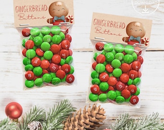 Op de afbeelding: Twee transparante zakjes gevuld met rode en groene snoepjes, met het label "Gingerbread Buttons". Elk zakje heeft een bruine papieren topper met een peperkoekmannetje. Feestelijke traktaties.