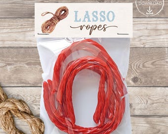 Puede incluir: Una bolsa de plástico transparente con cuerdas de regaliz rojas. La etiqueta dice "LASSO ropes" en escritura azul, con una ilustración de cuerda. También se ve un nudo de cuerda.