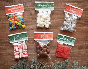 May include: Six clear plastic bags with colorful candy and labels. The labels are red and green with white text. The labels read "gingerbread buttons", "snowman poop", "santa kisses", "elf pillows", "reindeer noses", and "polar bear food".