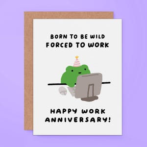 May include: A white greeting card featuring a green frog wearing a pink and white striped party hat, sitting at a desk with a computer and mouse. The text reads BORN TO BE WILD FORCED TO WORK and HAPPY WORK ANNIVERSARY in black lettering.