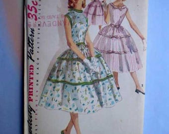 Może przedstawiać: Koperta z wykrojem krawieckim vintage Simplicity na sukienkę, rozmiar 12, biust 30, w cenie 35 centów. Ilustracja przedstawia sukienkę bez rękawów w kwiatowy wzór z warstwową spódnicą oraz drugi widok sukienki w paski z warstwową spódnicą.