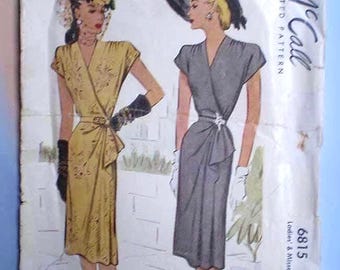 May include: A vintage McCall 6815 sewing pattern envelope featuring illustrations of two wrap-style dresses. One dress is yellow with a subtle pattern, and the other is solid grey. Both dresses have short sleeves, V-necklines, and waist detailing.