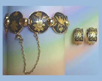 May include: A gold-tone bracelet and matching clip-on earrings set. The bracelet features circular black links with intricate gold floral and bird engravings, connected by small gold spheres and a delicate safety chain.