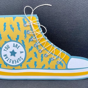 May include: Yellow and blue paper craft of a high-top sneaker with white laces. The sneaker has a lightning bolt pattern and a white circle with the text "You Are A Superstar" in blue.
