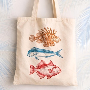 Canvas tote bag with three illustrated saltwater fish stacked vertically in orange, blue, and red, giving it a bold coastal nautical look