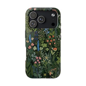 Pu&ograve; includere: Una custodia per smartphone con sfondo verde scuro e un denso motivo botanico di fiori selvatici, foglie e steli in tonalit&agrave; rosa, blu, arancione e verde chiaro, che circonda l'area nera del modulo fotocamera.