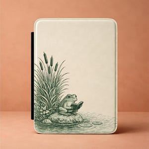 May include: A cream-colored tablet case featuring a detailed green illustration of a frog reading a book while sitting on a rock in a pond. The design includes cattails and lily pads, creating a nature-themed aesthetic.