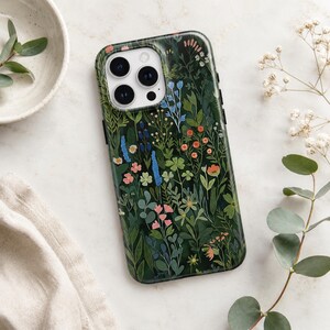 Pu&ograve; includere: Una cover per smartphone verde scuro con un'illustrazione botanica dettagliata di vari fiori selvatici e fogliame nei toni del rosa, arancione, blu e bianco. La cover presenta un ritaglio per un sistema a tripla fotocamera in alto a sinistra.