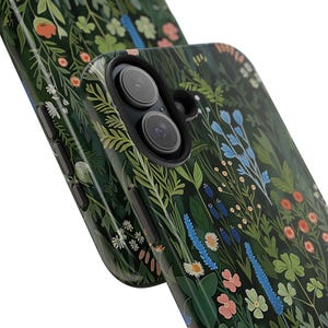 Glossy phone case with a dense botanical illustration of clovers and wildflowers on a dark green background, giving it a woodland cottagecore feel