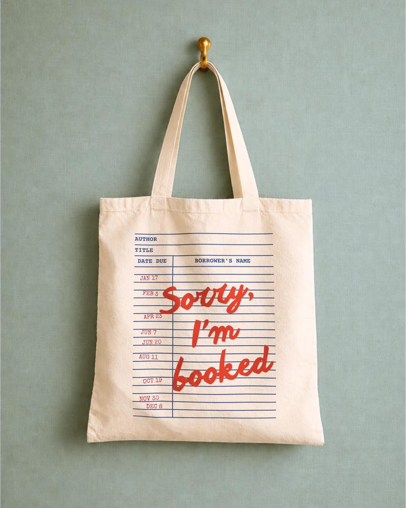Canvas tote bag with a vintage library card design and red stamped dates, featuring handwritten “sorry i’m booked” giving it a nostalgic bookish feel.