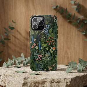 Pu&ograve; includere: Una custodia per smartphone con sfondo verde scuro e un denso motivo botanico colorato di fiori di campo, foglie e steli in tonalit&agrave; blu, rosa, arancione e verde chiaro, che include un ritaglio per la fotocamera a tripla lente in alto.