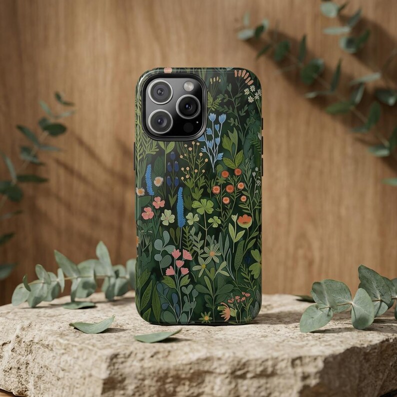 Pu&ograve; includere: Una custodia per smartphone con sfondo verde scuro e un denso motivo botanico colorato di fiori di campo, foglie e steli in tonalit&agrave; blu, rosa, arancione e verde chiaro, che include un ritaglio per la fotocamera a tripla lente in alto.