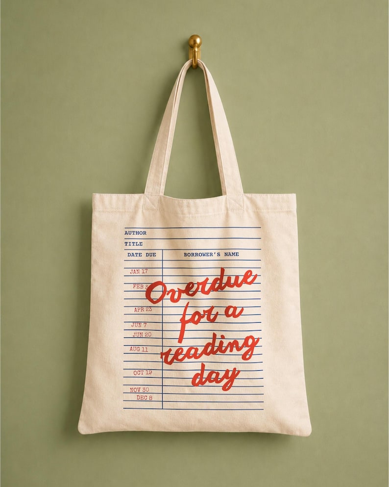 Canvas tote bag with a vintage library checkout card design and red script lettering that says “Overdue for a Reading Day”, giving it a nostalgic bookish style