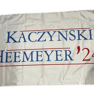 May include: A white flag with the text "KACZYNSKI HEEMEYER '24" in blue and red lettering.