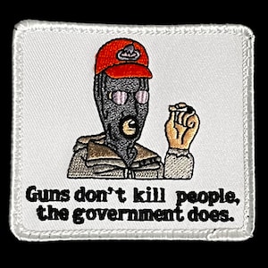 Op de afbeelding: Geborduurde patch met een figuur in een bivakmuts en een rode pet, die een klein voorwerp vasthoudt. De patch heeft de tekst "Guns don't kill people, the government does." op een witte achtergrond met een gestikte rand.
