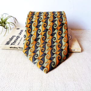 May include: A necktie featuring a repeating tessellated pattern of seahorses in shades of orange, sage green, and dark charcoal gray. The seahorses are arranged in an interlocking design that covers the entire surface of the pointed fabric accessory.
