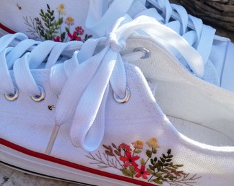 Witte canvas schoenen, wilde bloemen, grassen en bont borduursel van groene bladeren