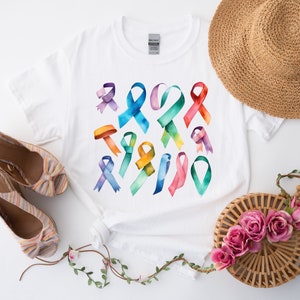 Peut inclure: T-shirt blanc avec un motif aquarelle color&eacute; de plusieurs formes de rubans. Les rubans sont dans des tons de rose, bleu, vert, jaune et violet.