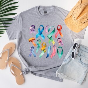 Peut inclure: Un t-shirt gris avec un motif aquarelle color&eacute; de plusieurs formes de rubans. Les rubans sont dans des tons de bleu, vert, jaune, orange, rouge, rose et violet.