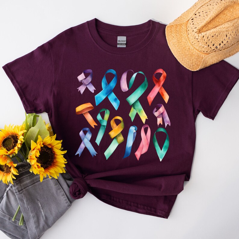 Peut inclure: Un t-shirt marron avec un motif aquarelle color&eacute; de plusieurs formes de rubans. Les rubans sont dans des tons de rose, bleu, vert, jaune et violet.