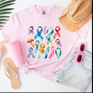 Peut inclure: Un t-shirt rose avec un motif aquarelle color&eacute; de plusieurs formes de rubans. Les rubans sont dans des tons de bleu, vert, jaune, orange, rose et violet.