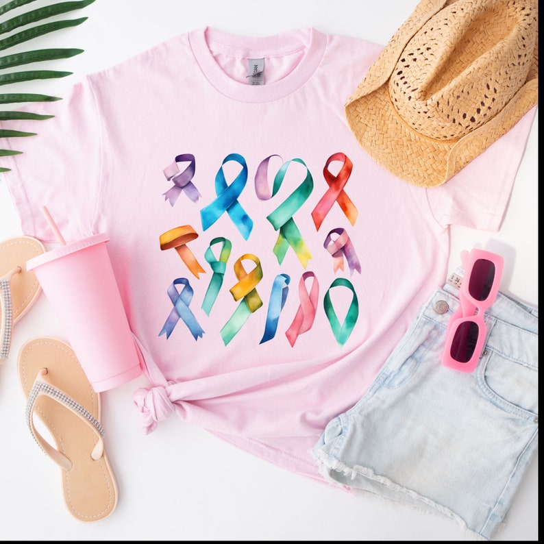 Peut inclure: Un t-shirt rose avec un motif aquarelle color&eacute; de plusieurs formes de rubans. Les rubans sont dans des tons de bleu, vert, jaune, orange, rose et violet.