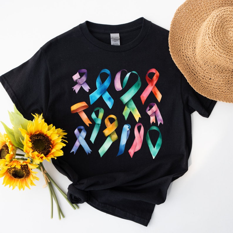 Peut inclure: T-shirt noir avec un motif aquarelle color&eacute; de plusieurs rubans de sensibilisation. Les rubans sont dans des tons de rose, bleu, vert, jaune et violet.