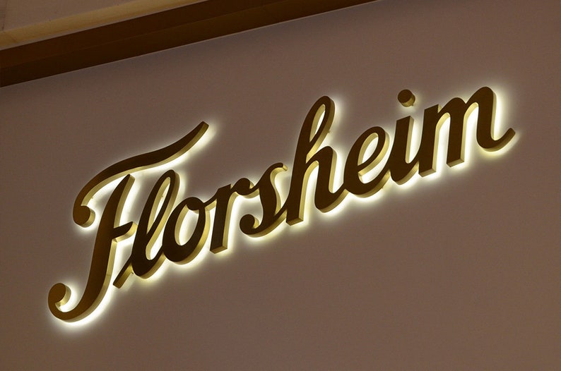 May include: A gold-colored, illuminated sign with the word "Florsheim" in a cursive script.