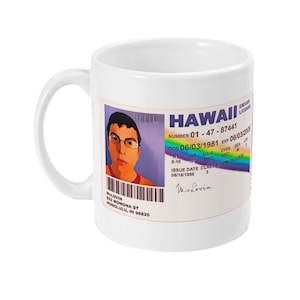 May include: White ceramic mug featuring a colourful Hawaii driving licence printed on it. The licence shows a cartoon portrait of a person named McLovin with a date of birth of 06/03/1981. The licence number is 01-47-87441.