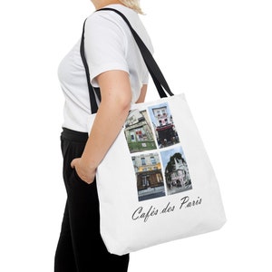 May include: White canvas tote bag with black handles and a collage of four photos of Parisian cafes. The text "Cafés des Paris" is printed in black at the bottom of the bag.