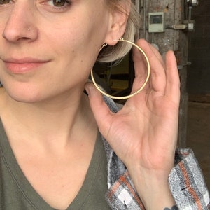 May include: A woman with short blonde hair wearing a green v-neck shirt and a gray and white plaid shirt. She is wearing large gold hoop earrings.