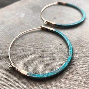 May include: A pair of large, gold hoop earrings with a turquoise blue enamel finish. The earrings have a simple, modern design.