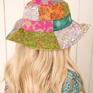 May include: A green, pink and orange patchwork bucket hat with a paisley pattern. The hat is made of fabric and has a wide brim.