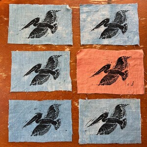 Puede incluir: Seis cuadrados de tela con siluetas de pelícanos negros impresas en ellos. Cuatro de los cuadrados son de color azul claro y dos son de color naranja claro.