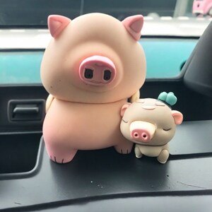 Könnte beinhalten: Zwei rosa und braune Schweinefiguren. Das größere Schwein steht mit leicht gespreizten Vorderbeinen. Das kleinere Schwein sitzt mit den Vorderbeinen unter dem Körper. Beide Schweine haben geschlossene Augen und rosa Schnauzen.