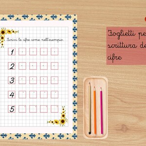 Può includere: Un foglio di lavoro con i numeri da 1 a 5, ciascuno seguito da caselle vuote per esercitarsi a scrivere. Il testo "Scrivi le cifre come nell'esempio" è in alto. Un piccolo vassoio di legno contiene tre matite. Un pulsante di download PDF è in alto a destra.