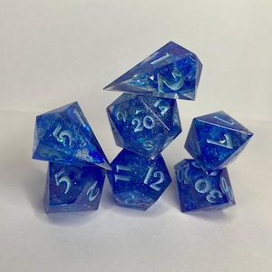 May include: Set of six blue and white iridescent dice with glitter embedded in the resin. The dice are numbered 1-20 and are shaped like a variety of polyhedrons.